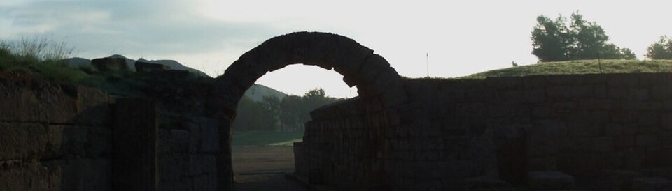 Blick auf das antike Wettlauffeld in Olympia mit Torbogen.
